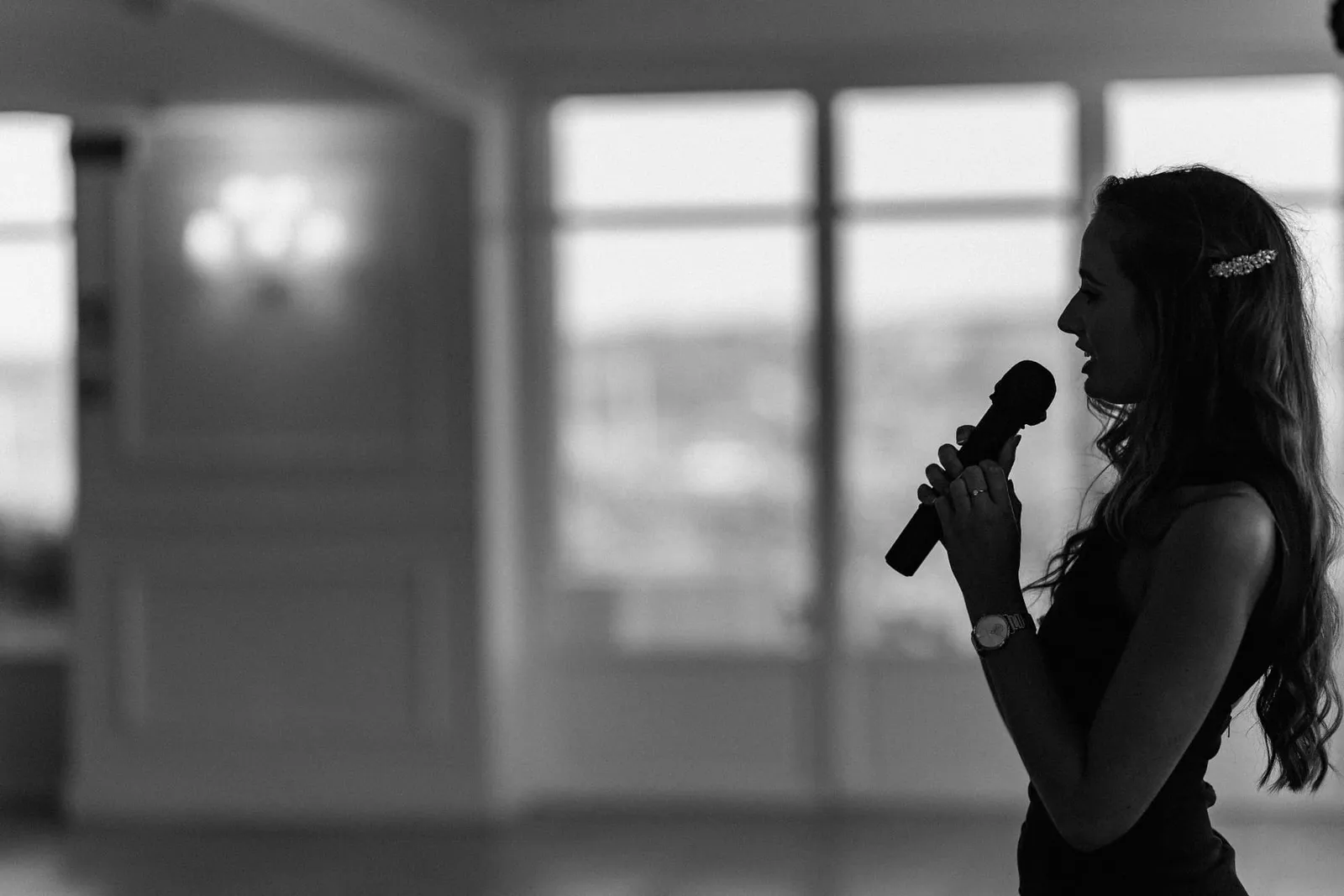 Black and white silhouette of Sally Hall singing by tall windows