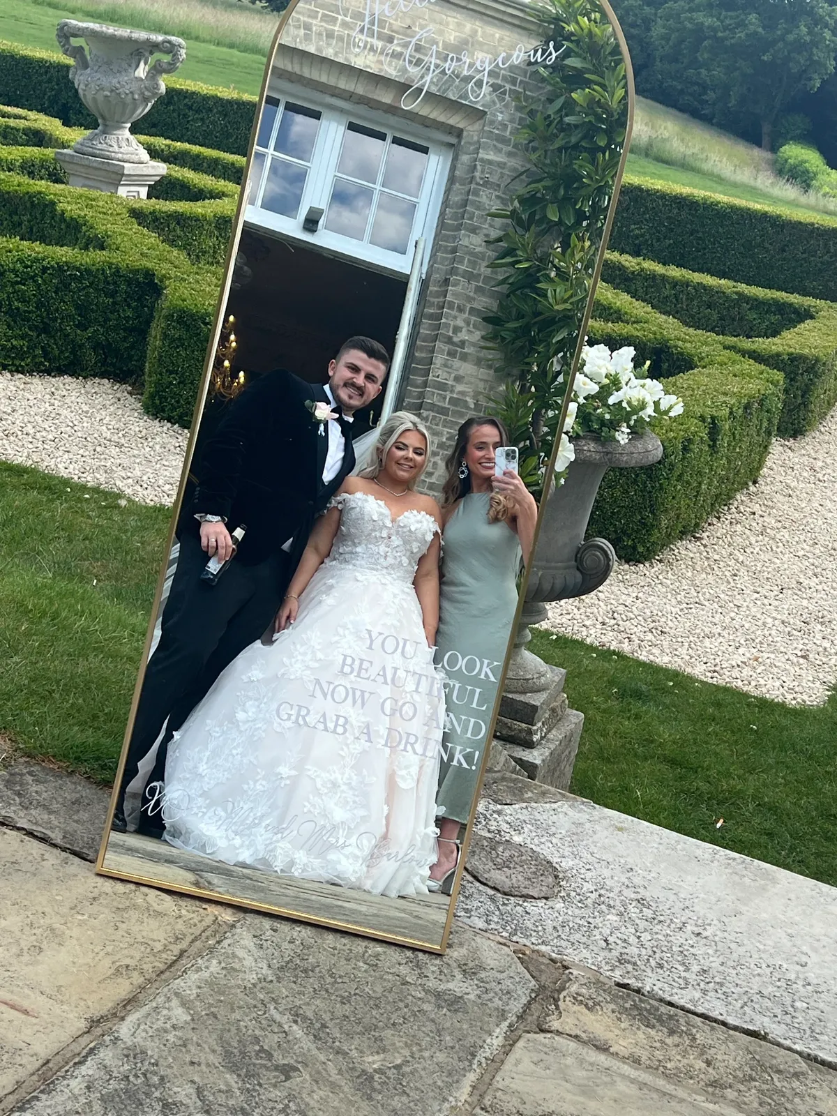 Sally Hall taking a mirror photo with a bride and groom in a formal garden